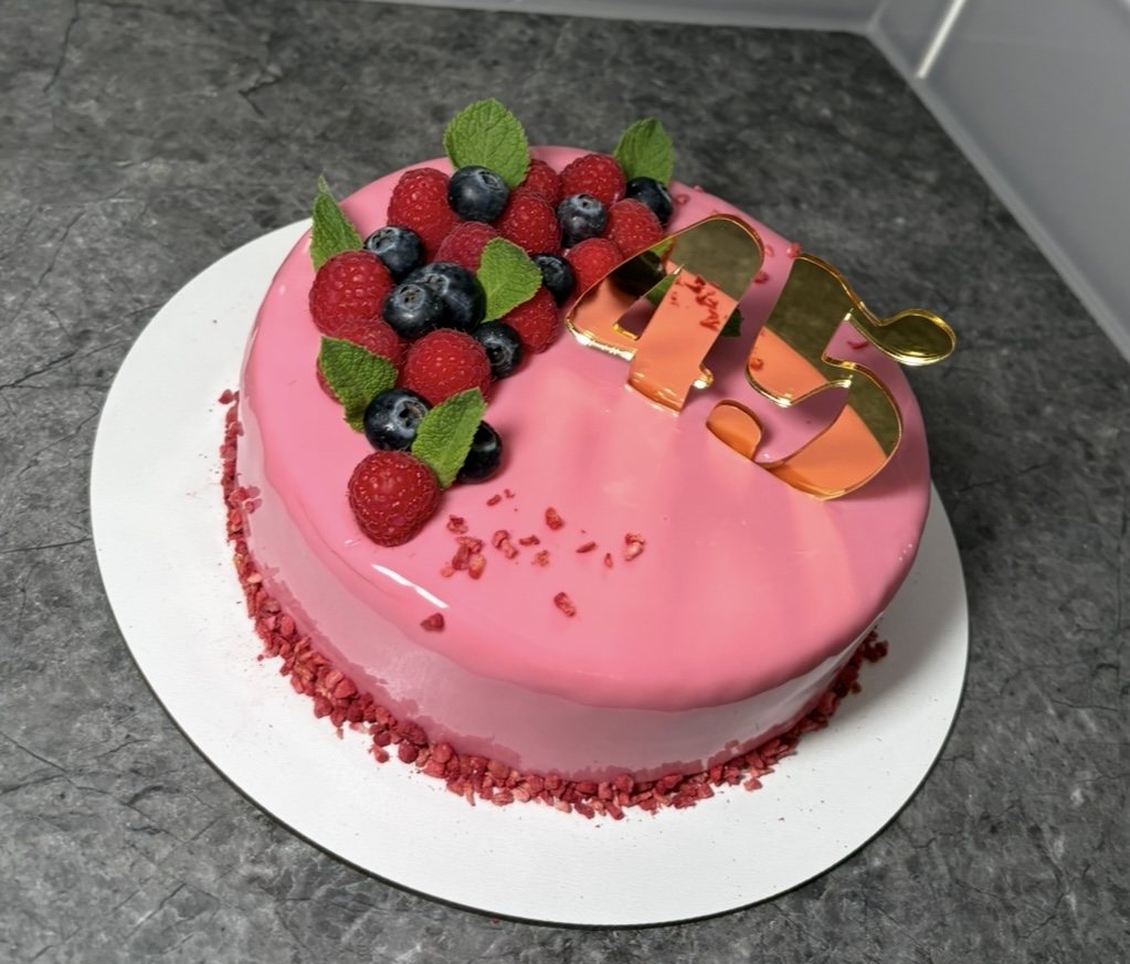 Pink mirror glaze mousse cake with raspberries, blueberries and a gold topper