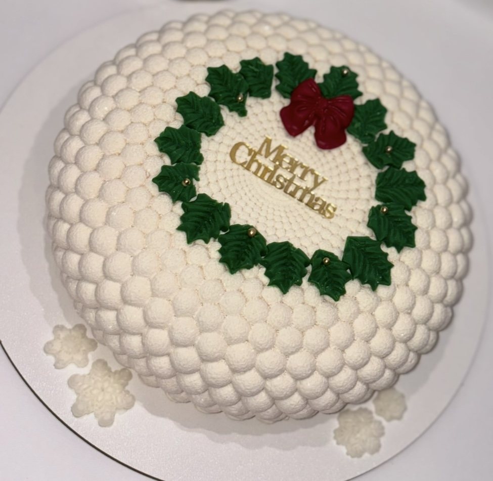 White textured mousse cake with a Merry Christmas wreath decoration